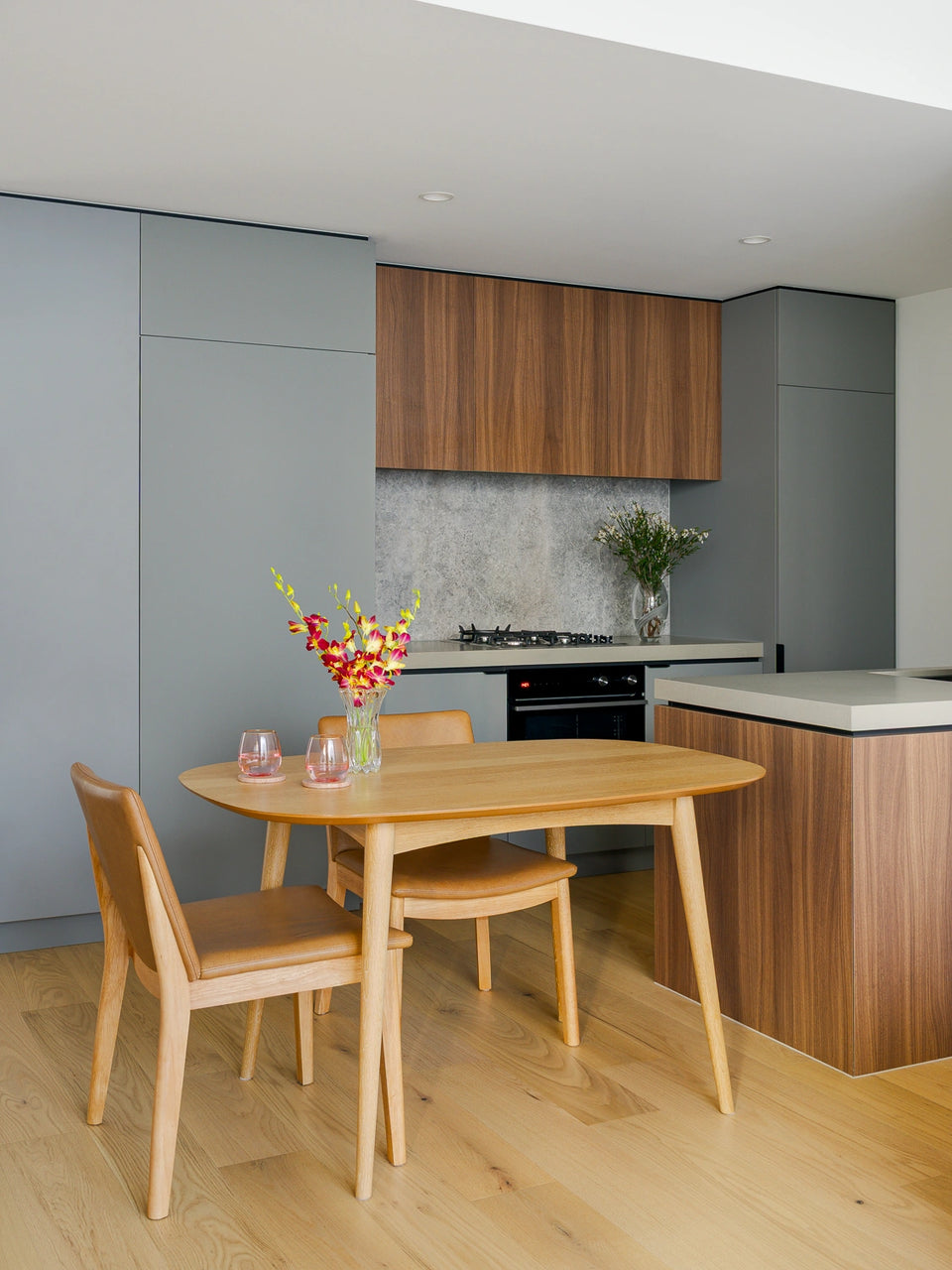 Modern kitchen with wooden dining table and chairs, featuring a vase of flowers.