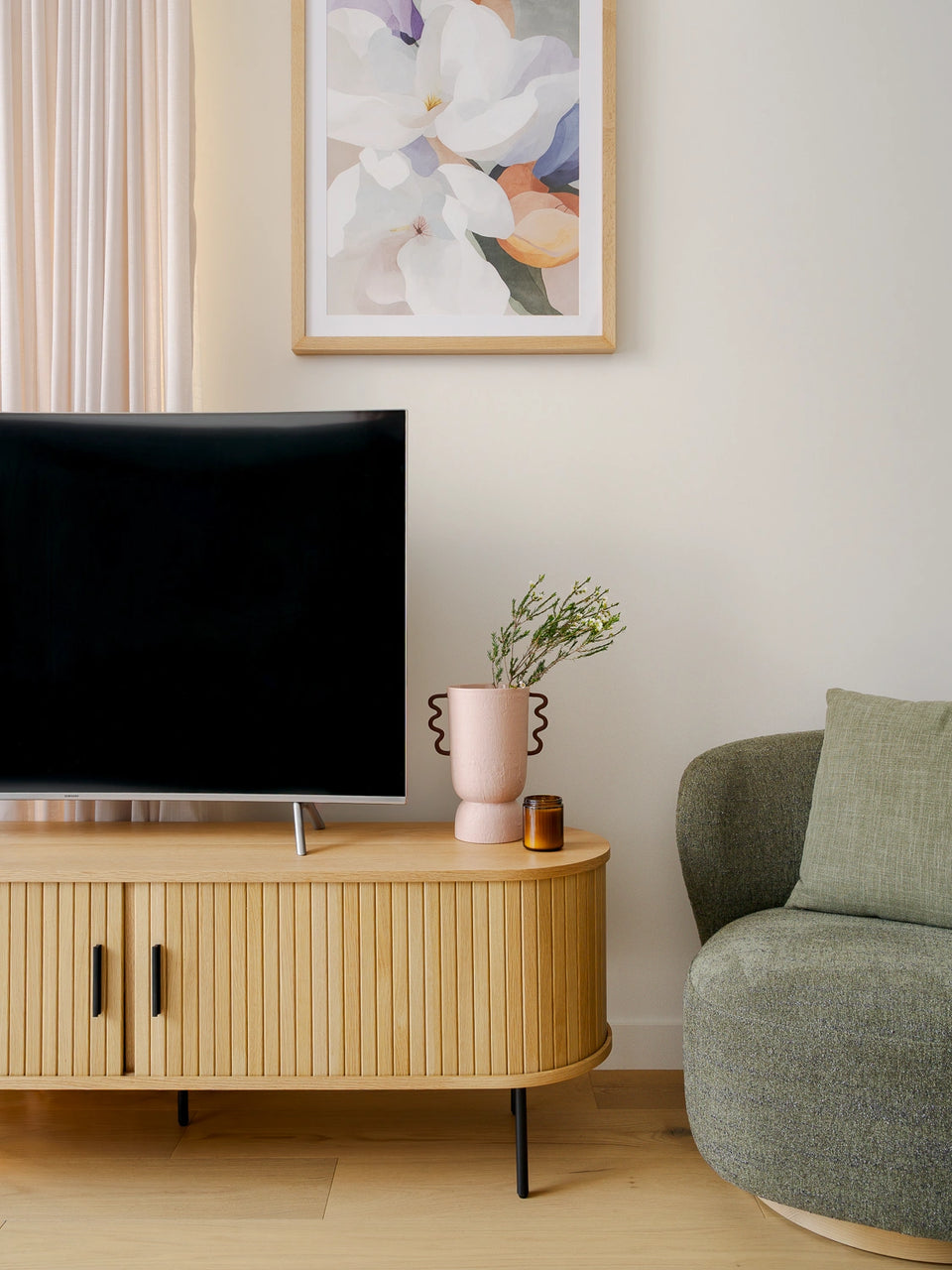 Modern living room with a television on a wooden stand, a green sofa, and a floral painting on the wall.