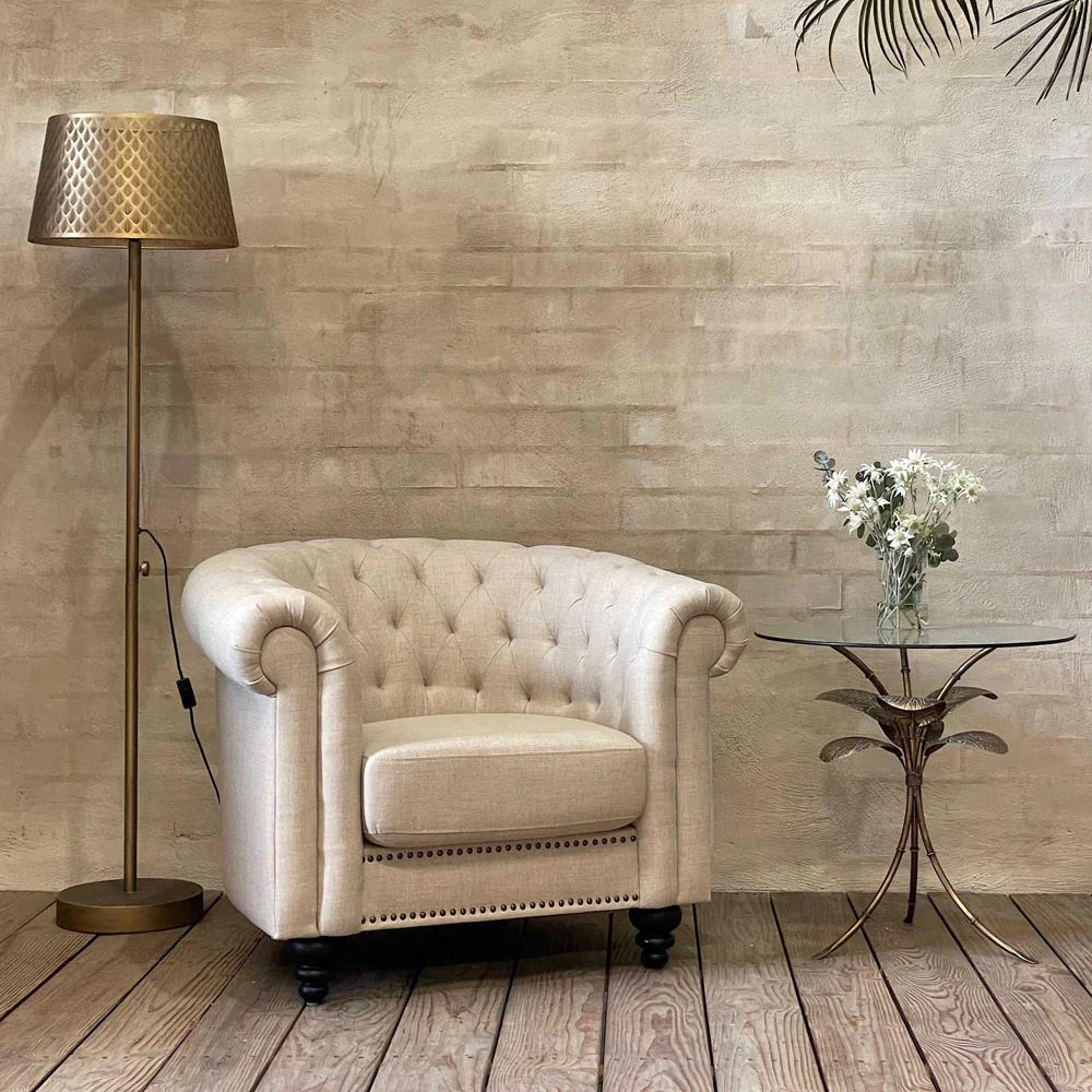 Amari Gold Leaf Side Table styled beside an armchair, featuring a glass top and elegant botanical-inspired base in a warm gold tone.
