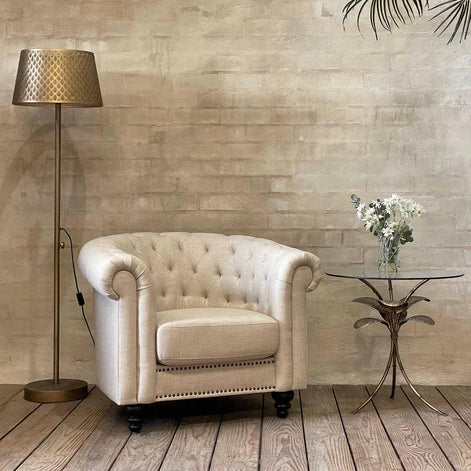 Amari Gold Leaf Side Table styled beside an armchair, featuring a glass top and elegant botanical-inspired base in a warm gold tone.