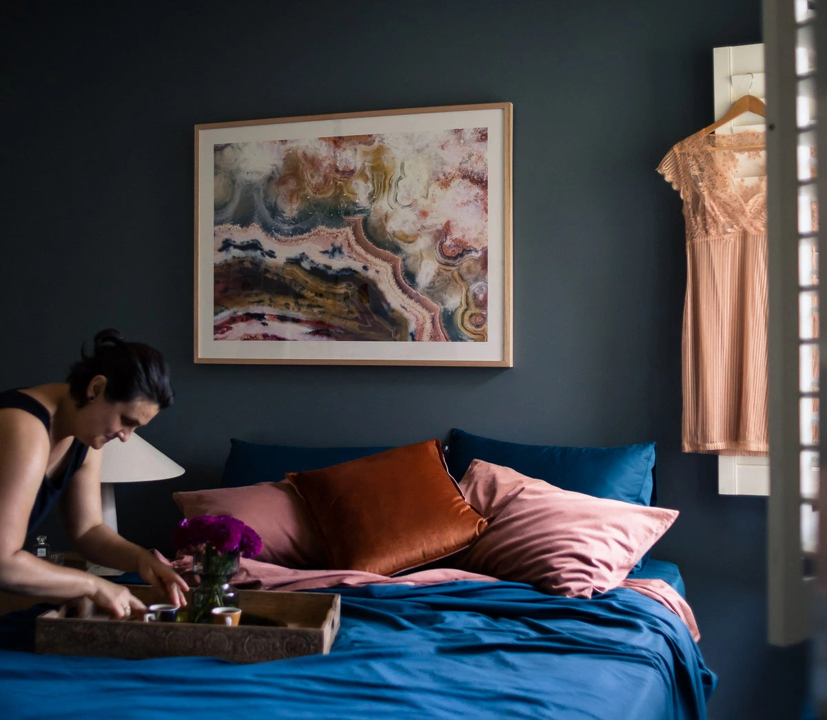 Anica arranging flowers on a bed with colorful pillows and a large abstract painting on the wall. Reservoir project.