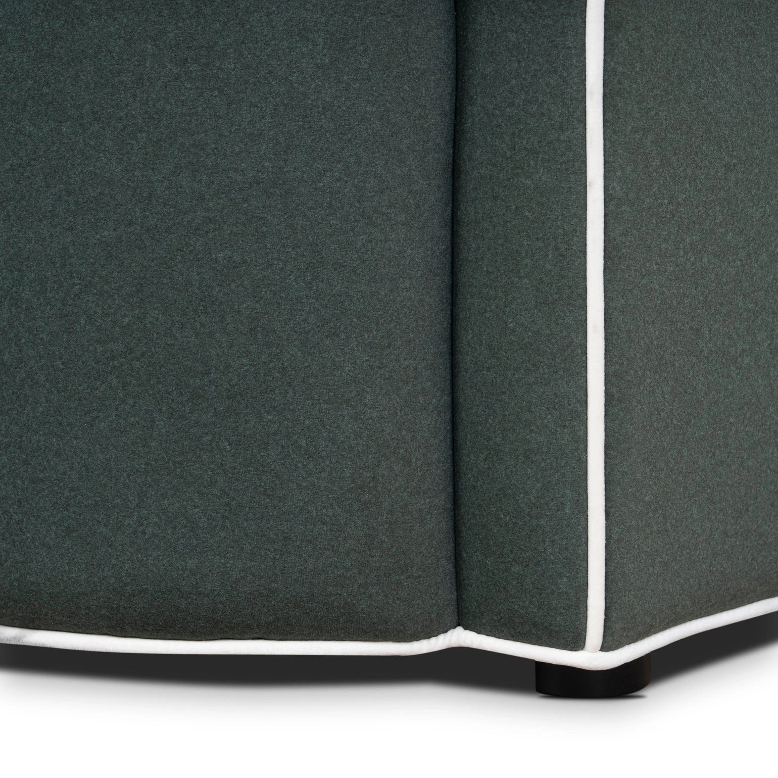 Close-up of a dark gray upholstered corner piece with white piping on a white background