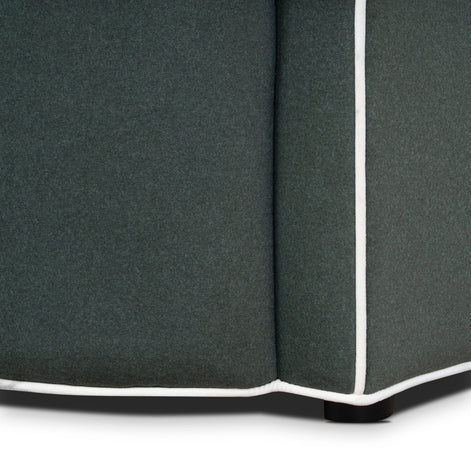 Close-up of a dark gray upholstered corner piece with white piping on a white background