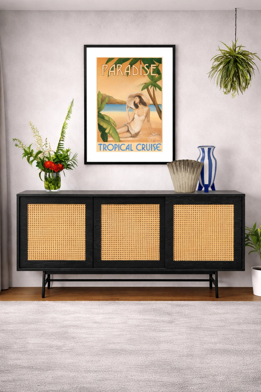 Framed tropical cruise poster above a black console table with wicker doors.