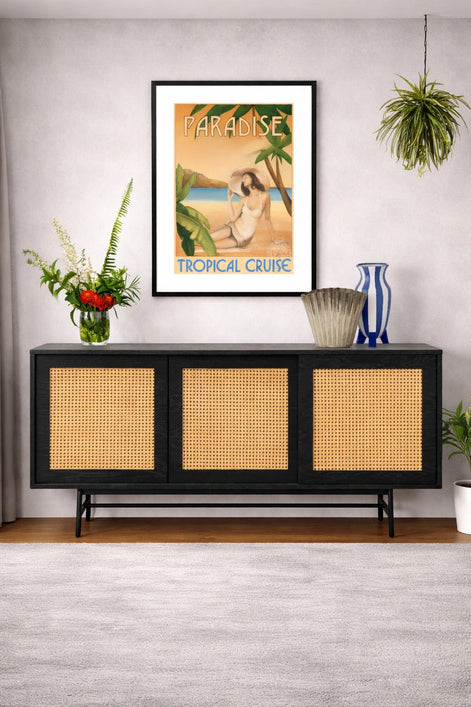 Framed tropical cruise poster above a black console table with wicker doors.
