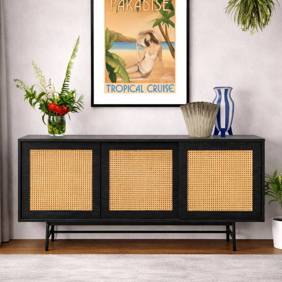 Framed tropical cruise poster above a black console table with wicker doors.