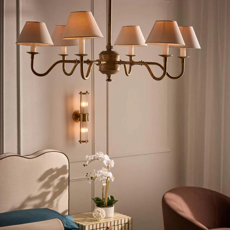 Chandelier hanging above a sofa with a wall sconce and table with flowers in a room.