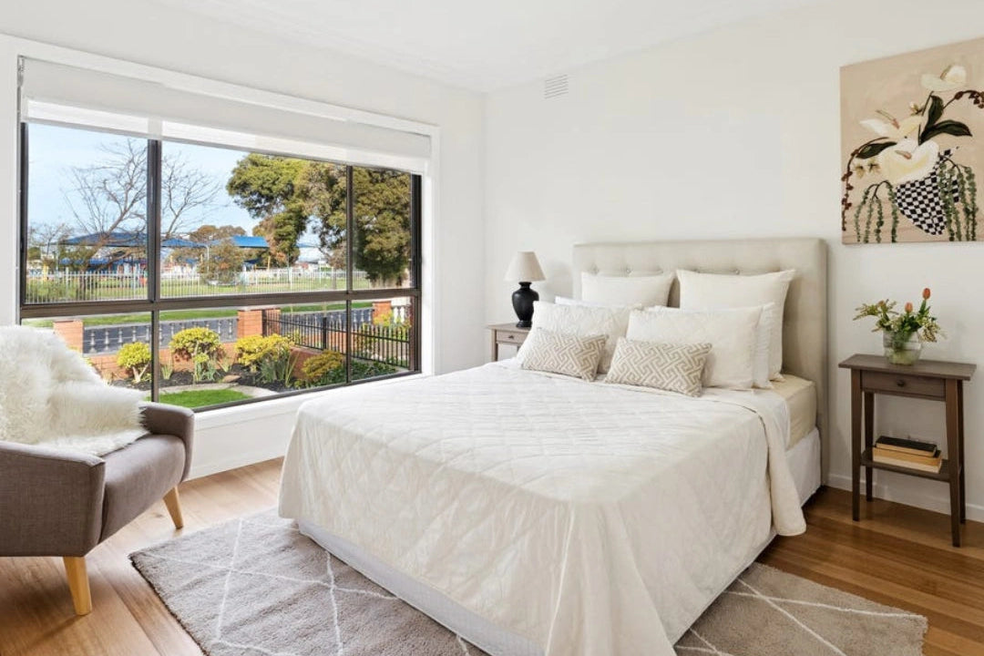 Modern bedroom, Reservoir Victoria styled queen bed, armchair, and large window view. Neutrals and homely softened by a floor rug.