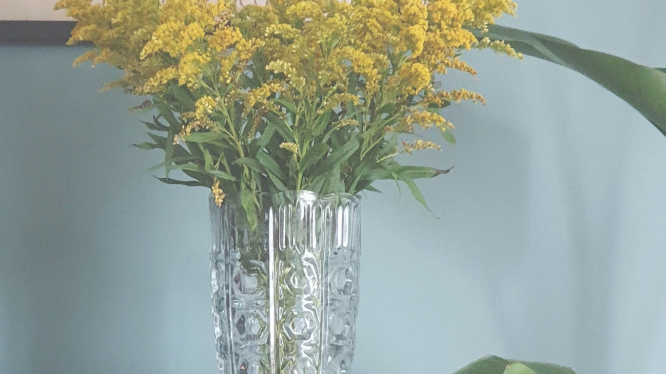 Clear glass vase with yellow flowers against a light blue background