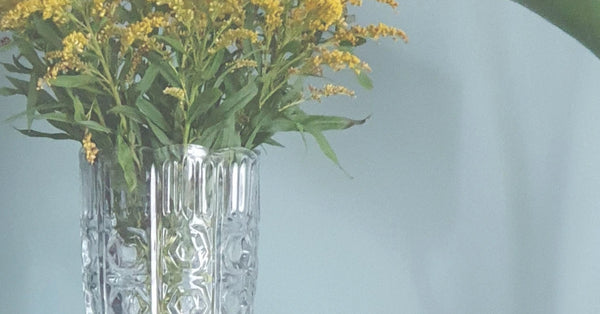 Clear glass vase with yellow flowers against a light blue background